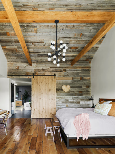 Bedroom with vintage wood wall and ceiling cladding. Reclaimed Oak beams and flooring with natural color. 