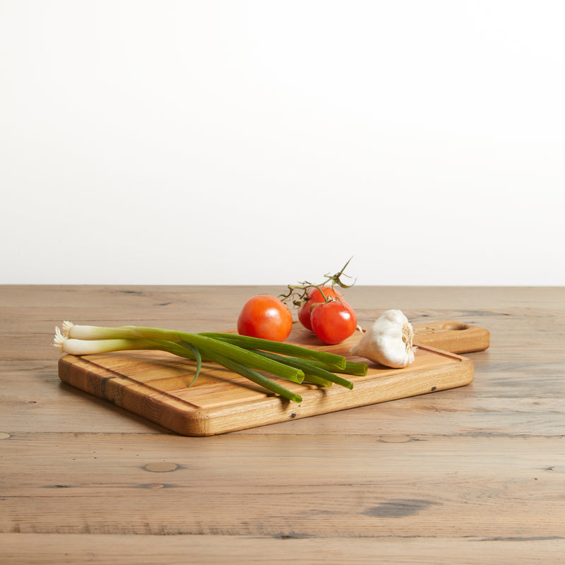 Reclaimed Oak rectangle cutting board with handle. Natural oak color with grain. Shown with vegatables