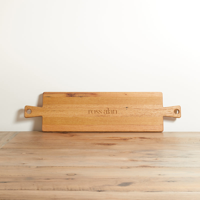 Long rectangle charcuterie board with handle on both ends. Relclaimed oak with natural color and wood grains. Leaning against white wall