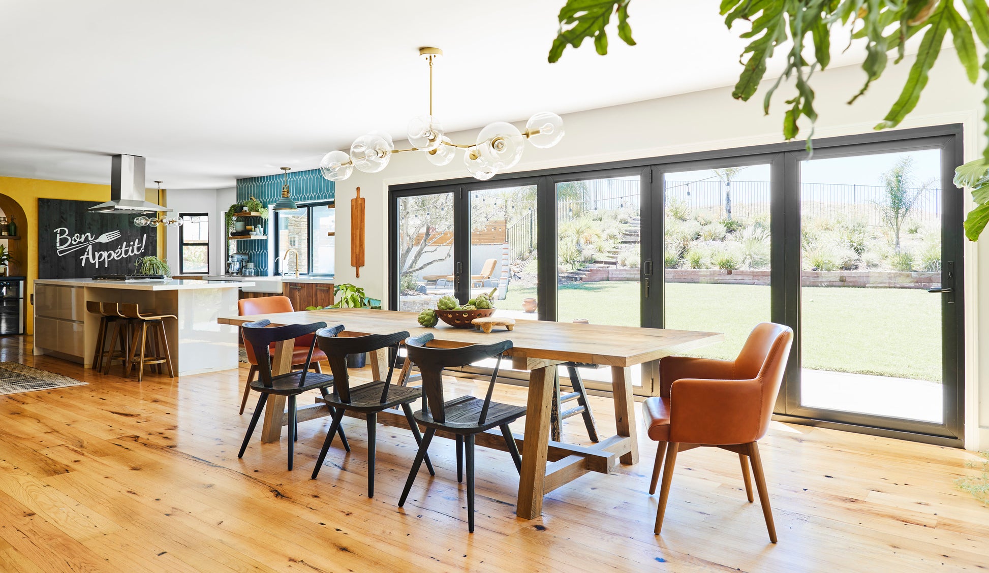 Reclaimed oak farmhouse table in front of windows in a dining room. Shown with back wood dining chairs and brown leather armed dining chairs.